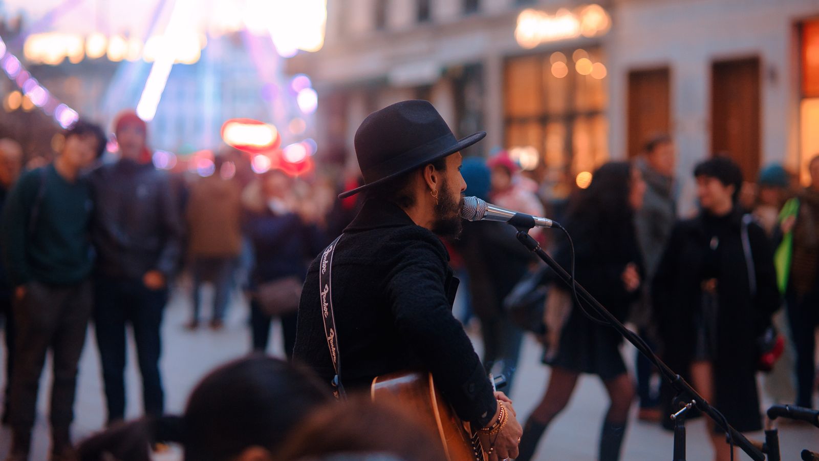 Músico callejero cantando con guitarra ante el público en una calle peatonal de noche
