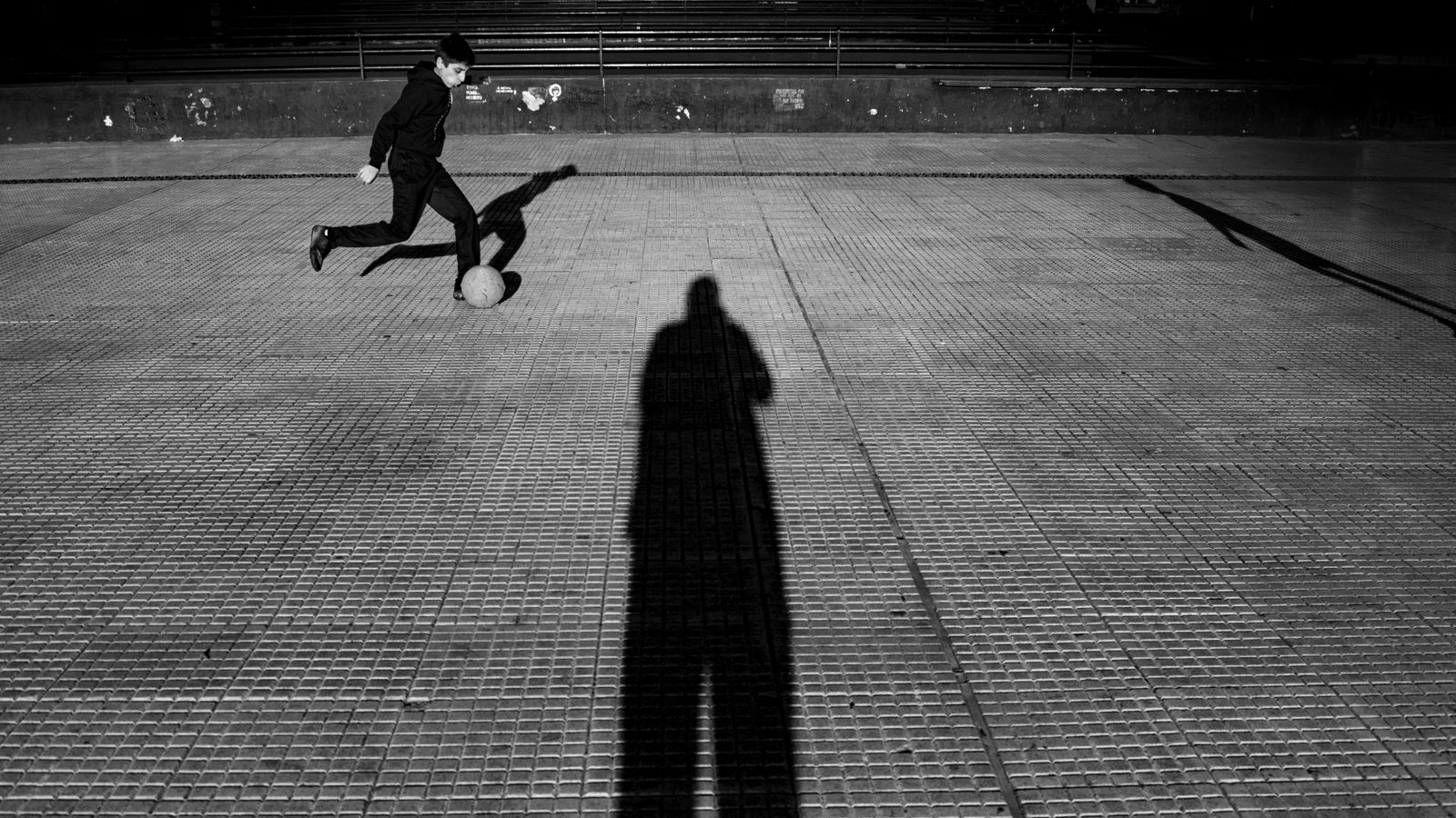Un nene juega con una pelota de fútbol en la vereda, en blanco y negro