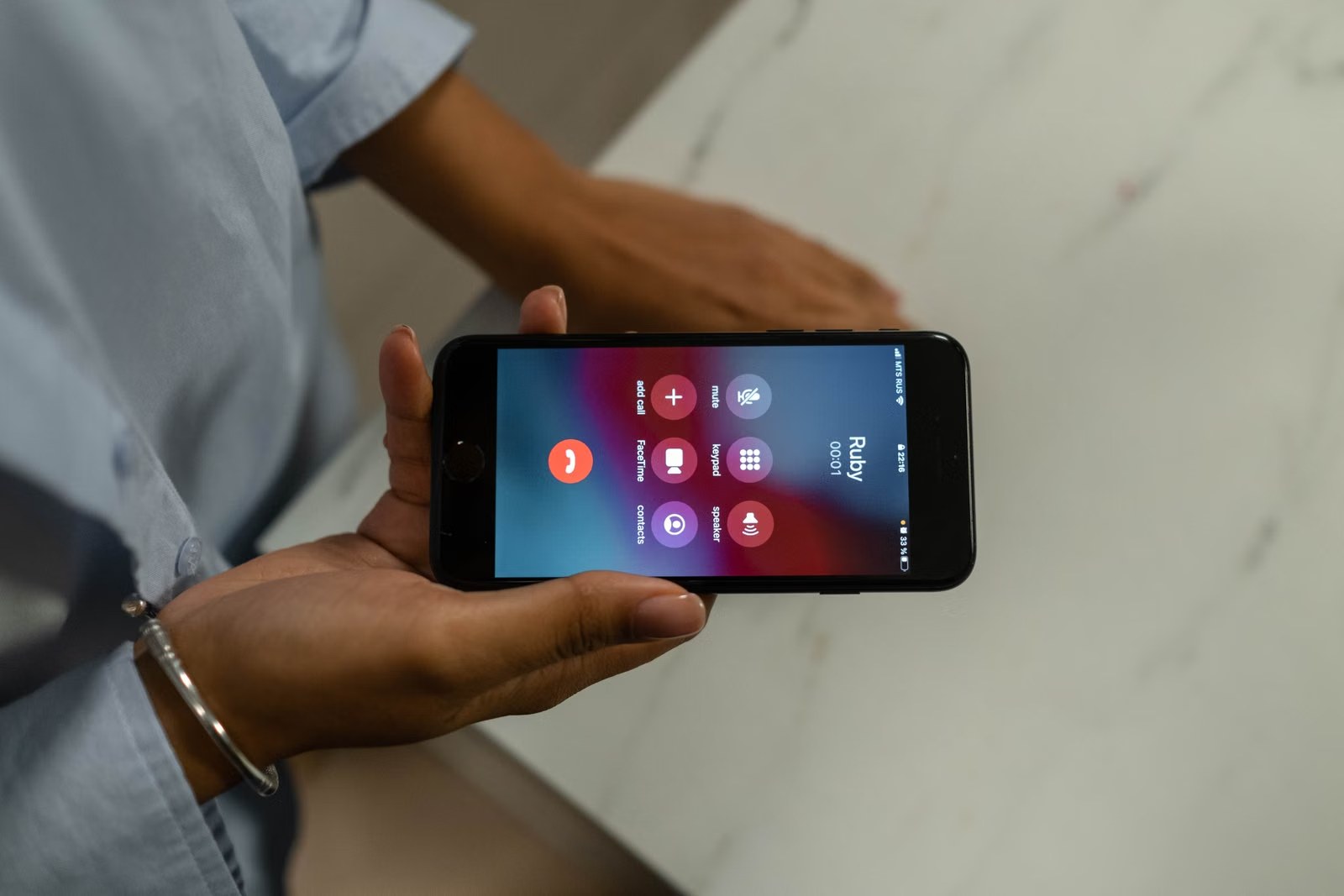 Mano apoyada en una mesa con un celular que muestra la pantalla de una llamada