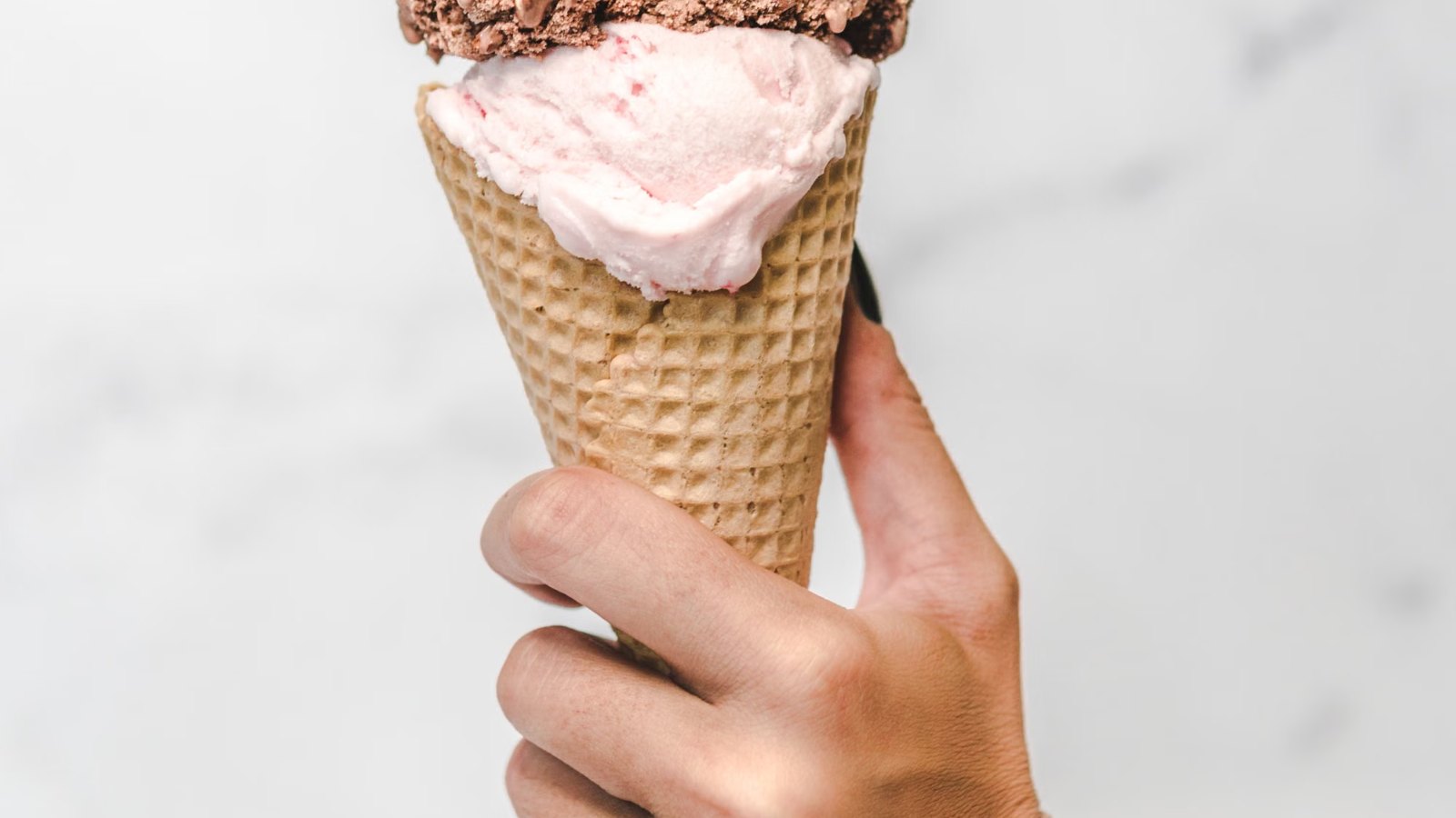 Mano sosteniendo un cucurucho de helado con dos gustos