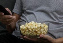 Persona con un bowl de pochoclos y el control remoto en una noche de películas
