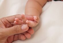 Mano de una persona adulta sosteniendo la mano de un bebé recién nacido