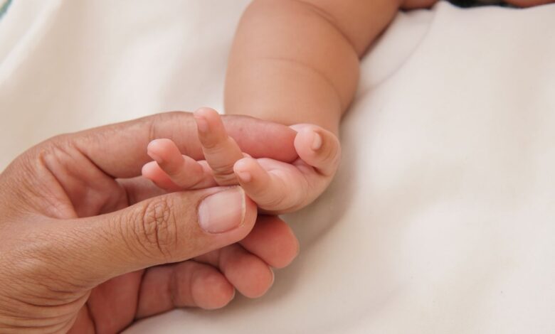 Mano de una persona adulta sosteniendo la mano de un bebé recién nacido