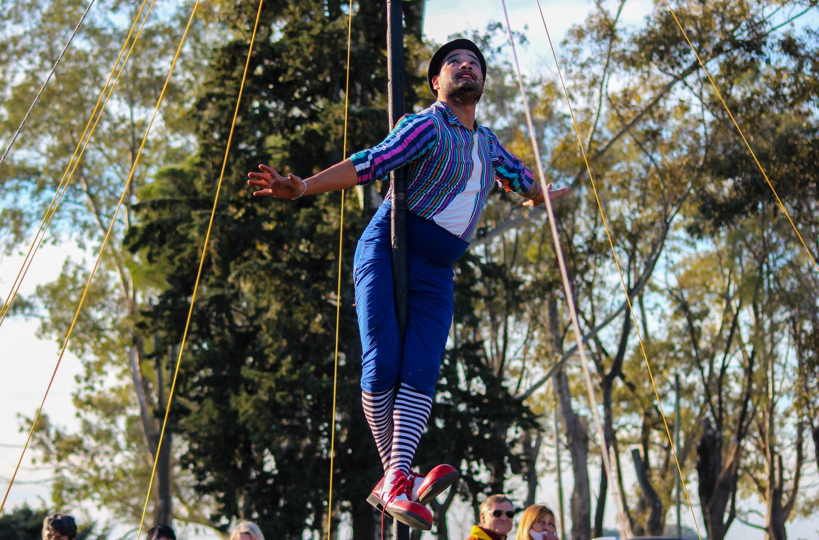 Artista de circo hace equilibrio sobre una cinta tensada al aire libre entre árboles