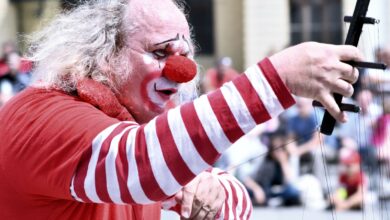 Payaso con nariz roja y traje a rayas actúa con un micrófono frente al público en la calle