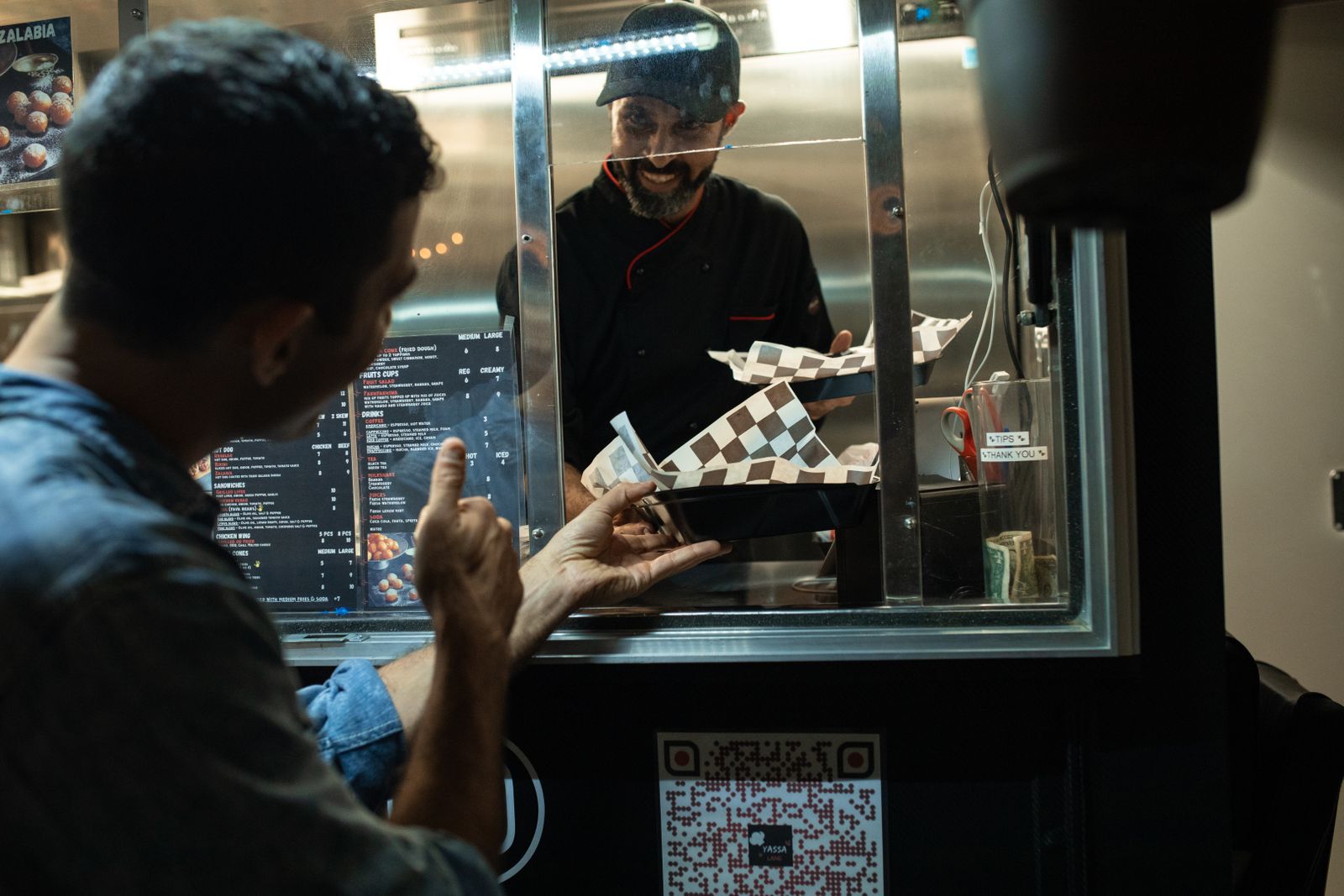 Persona haciendo un pedido en la ventanilla de un foodtruck de noche