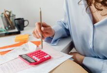 Mujer calcula gastos con una calculadora y papeles sobre el escritorio
