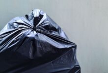 Bolsa de residuos negra cerrada apoyada contra una pared