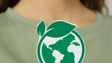 Mujer sostiene un adhesivo con el planeta Tierra dentro de una hoja verde, símbolo de sostenibilidad