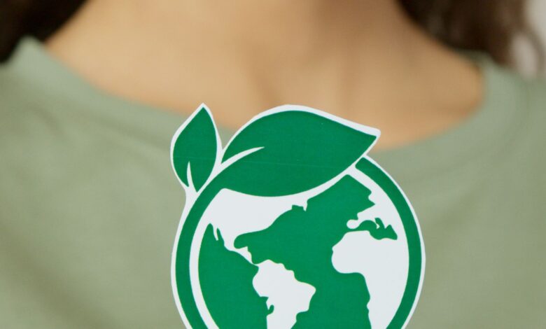 Mujer sostiene un adhesivo con el planeta Tierra dentro de una hoja verde, símbolo de sostenibilidad
