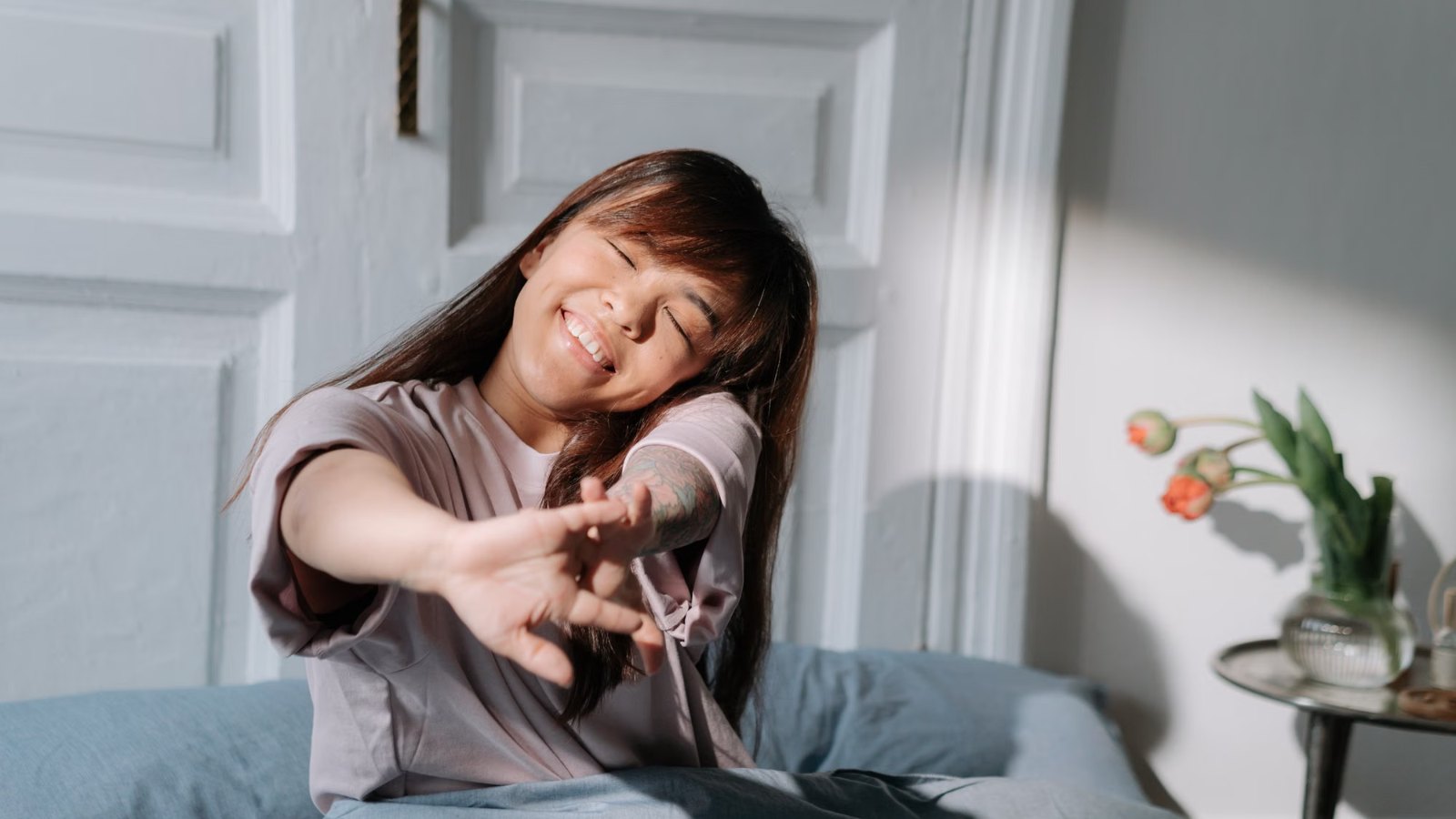 Mujer estirándose sentada en la cama, con luz de la mañana