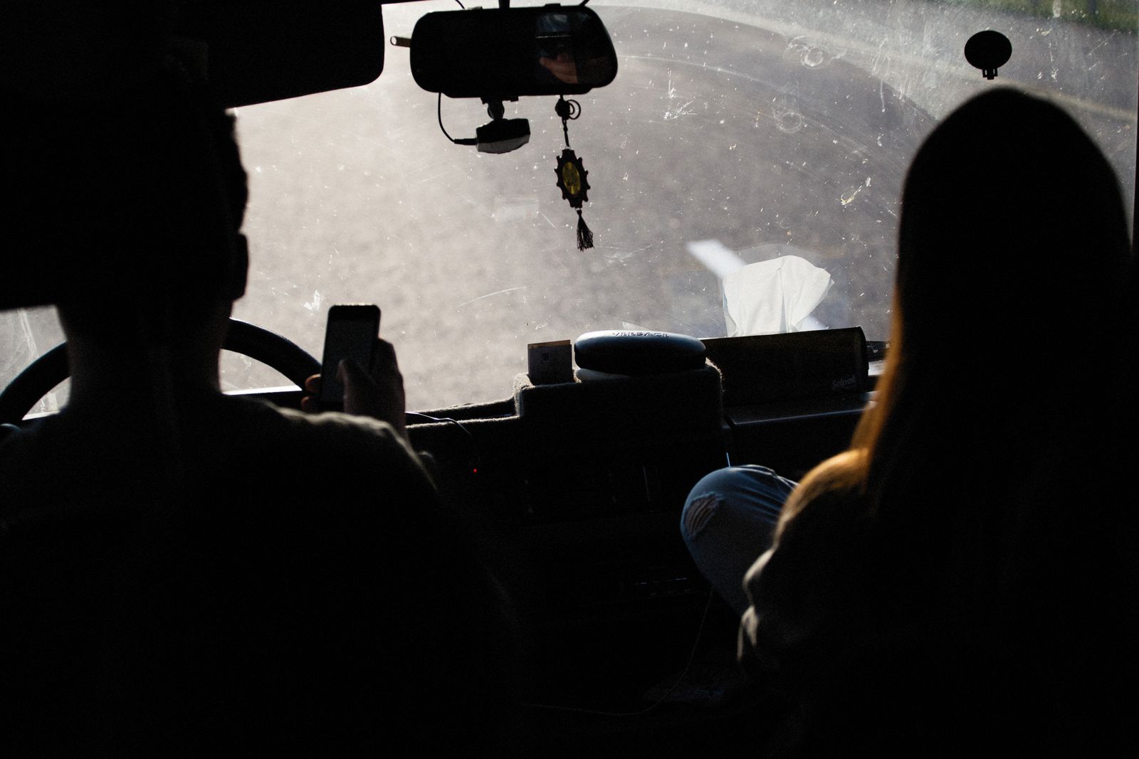 Conductor y pasajero dentro de un auto al atardecer, uno de ellos usa el celular