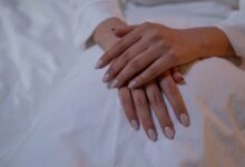 Manos con uñas nude prolijas apoyadas sobre una tela blanca