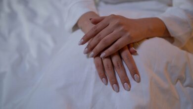 Manos con uñas nude prolijas apoyadas sobre una tela blanca