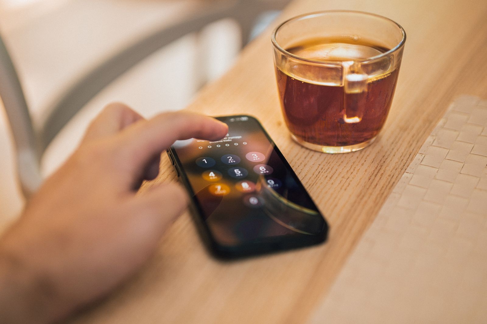 Mano desbloqueando un celular sobre una mesa de madera junto a una taza