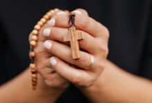 Manos que sostienen un rosario de madera con una cruz